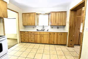 Kitchen with light countertops, white stove, light tile patterned floors, brown cabinets, and ornamental molding