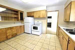 Kitchen with open shelves, light countertops, white appliances, light tile patterned floors, and brown cabinetry
