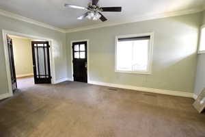 Carpeted entryway featuring crown molding, plenty of natural light, and ceiling fan