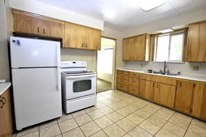 Kitchen featuring white appliances, light countertops, light tile patterned flooring, and brown cabinetry