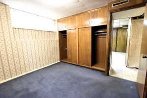 Unfurnished bedroom with dark carpet, a closet, and wallpapered walls