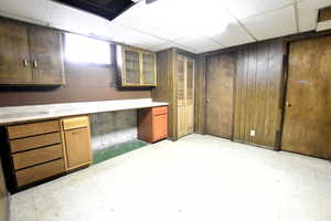 Below grade area featuring light floors, a drop ceiling, and wooden walls