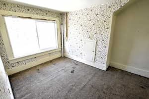 Unfurnished bedroom with wallpapered walls and carpet flooring