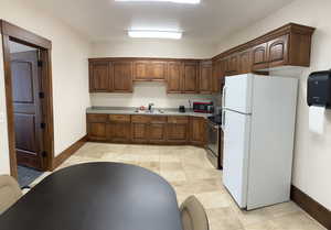 Kitchen with freestanding refrigerator, stainless steel electric stove, light countertops, and light tile patterned floors