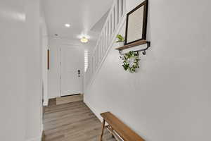 Hallway with light wood finished floors, stairway, and recessed lighting