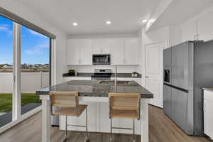 Kitchen with stainless steel appliances, white cabinetry, light wood-style floors, an island with sink, and recessed lighting