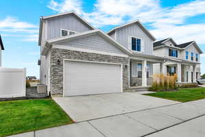 View of front facade with board and batten siding, a porch, concrete driveway, a front yard, and stone siding