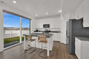 Kitchen with white cabinetry, light wood-style floors, a residential view, a center island with sink, and recessed lighting