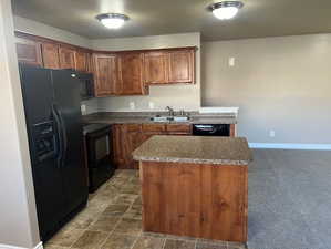 Kitchen featuring black appliances, a kitchen island, dark countertops, brown cabinetry, and a textured ceiling