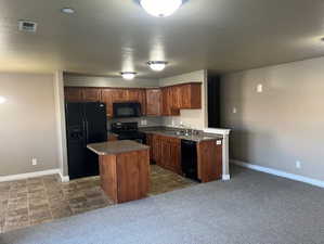 Kitchen featuring black appliances, dark countertops, a textured ceiling, a kitchen island, and dark carpet
