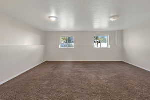 Unfurnished room featuring dark carpet, plenty of natural light, and a textured ceiling