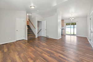 Unfurnished living room with a chandelier, stairway, and dark wood finished floors