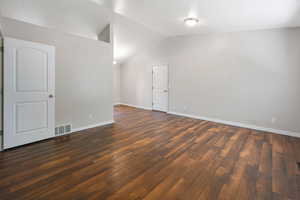 Spare room with dark wood-type flooring and lofted ceiling