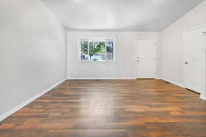 Empty room featuring dark wood-style flooring and baseboards