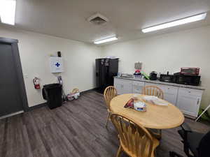 Kitchen with a textured ceiling, black appliances, dark wood-style flooring, light stone countertops, and white cabinetry