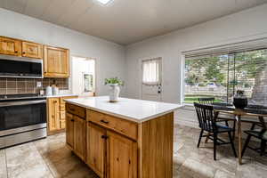 Kitchen with crown molding, stainless steel appliances, backsplash, a center island, and brown cabinets