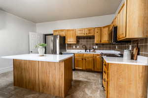 Kitchen with backsplash, a kitchen island, brown cabinetry, stainless steel appliances, and ornamental molding