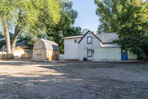 Back of property featuring a chimney, a storage unit, and roof with shingles