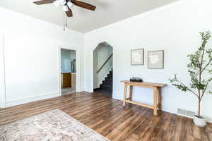Empty room with crown molding, dark wood finished floors, ceiling fan, and stairs