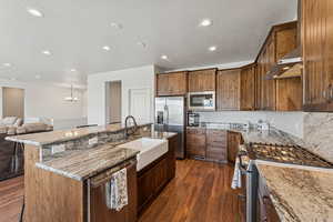 Kitchen with stainless steel appliances, dark wood-style flooring, an island with sink, light stone countertops, and a textured ceiling