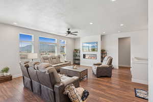 Living area featuring a glass covered fireplace, a textured ceiling, dark wood-type flooring, recessed lighting, and a ceiling fan