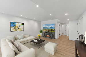 Living area with recessed lighting, light wood finished floors, and a warm lit fireplace. This has been virtually staged.