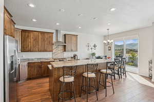 Kitchen featuring stainless steel appliances, a kitchen island, dark wood-style flooring, a breakfast bar area, and hanging light fixtures