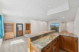 Kitchen with light wood finished floors, brown cabinetry, recessed lighting, open floor plan, and a peninsula