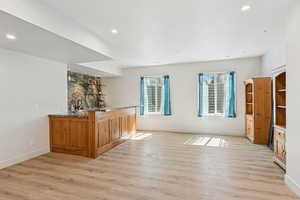 Indoor wet bar with brown cabinetry, light wood-type flooring, recessed lighting, and dark stone countertops