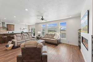 Living room featuring a glass covered fireplace, a textured ceiling, ceiling fan, hardwood / wood-style flooring, and a chandelier