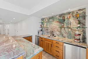 Indoor wet bar with recessed lighting, brown cabinetry, beverage cooler, and light stone countertops