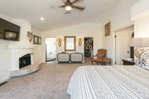 Bedroom featuring lofted ceiling, a walk in closet, a fireplace with raised hearth, carpet floors, and a ceiling fan