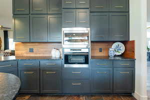 Kitchen with dark stone countertops, decorative backsplash, stainless steel appliances, and dark stone finish flooring