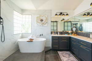 Full bathroom with tile walls, a soaking tub, vanity, dark tile patterned floors, and tasteful backsplash