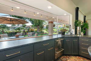 Bar featuring rail lighting, stainless steel dishwasher, and dark stone counters