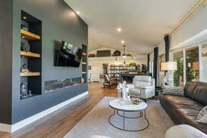 Living area with a glass covered fireplace, light wood finished floors, built in shelves, lofted ceiling, and recessed lighting
