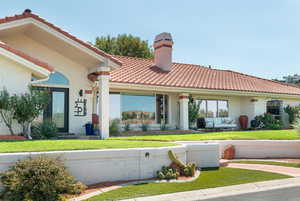 View of front of home featuring a tile roof, a chimney, stucco siding, and a front lawn