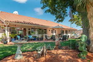Back of house featuring a patio area, a tiled roof, a chimney, and a lawn