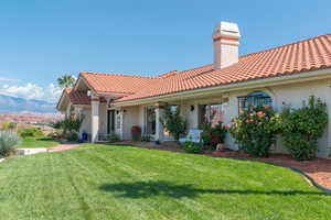 View of front of house with stucco siding, a front lawn, a chimney, and covered porch