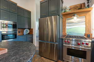 Kitchen featuring stainless steel appliances, dark stone counters, open shelves, dark stone finish floors, and decorative backsplash
