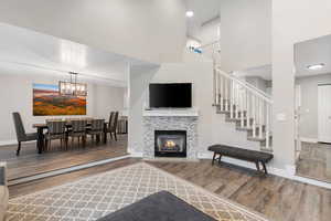 Living room featuring a towering ceiling, a tiled fireplace, wood finished floors, stairway, and a chandelier