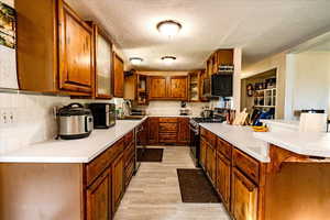 Kitchen featuring brown cabinets, appliances with stainless steel finishes, tasteful backsplash, a textured ceiling, and light countertops