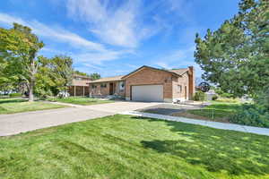 Ranch-style home featuring concrete driveway, brick siding, a chimney, an attached garage, and a front yard