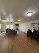 Living room featuring a fireplace, light wood finished floors, a textured ceiling, and a ceiling fan