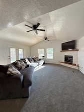 Living room with carpet floors, a large fireplace, a textured ceiling, lofted ceiling, and ceiling fan