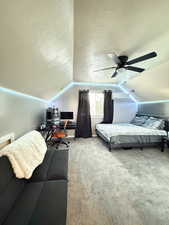 Carpeted bedroom featuring a desk, a textured ceiling, lofted ceiling, and ceiling fan