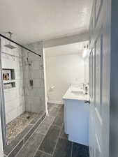 Bathroom featuring double vanity, a marble finish shower, a textured ceiling, and dark tile patterned floors