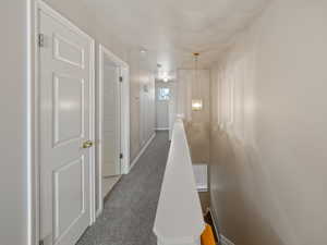 Hallway featuring an upstairs landing and dark carpet