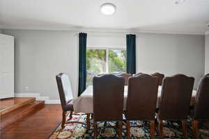 Dining room with ornamental molding and dark wood-style flooring