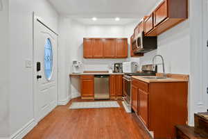 Kitchen featuring brown cabinetry, light countertops, appliances with stainless steel finishes, dark wood finished floors, and recessed lighting